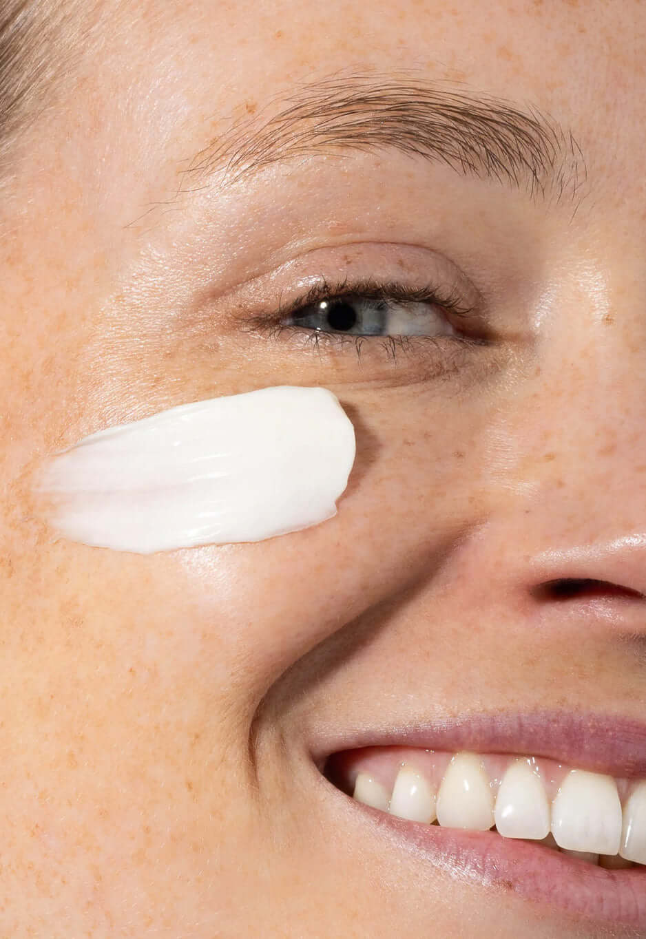 Close-up of a smiling woman with a stroke of white cream on her cheekbone