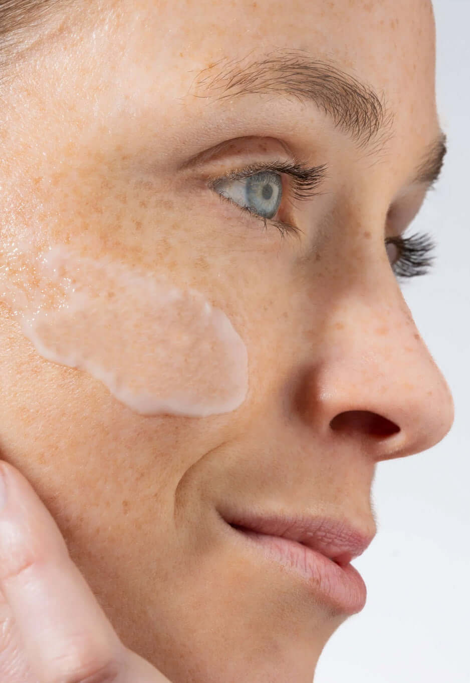 Side view of a woman's face with a smear of translucent serum on her cheek
