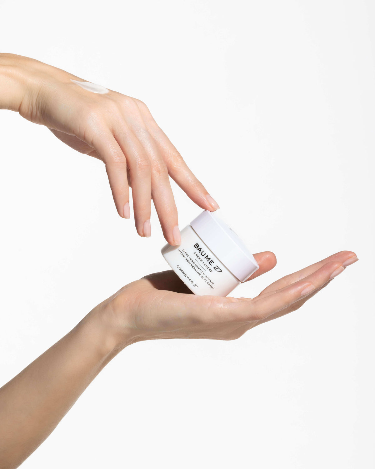 Jar of Baume 27 Soft Cream resting in an open palm, held by the fingertips of the other hand