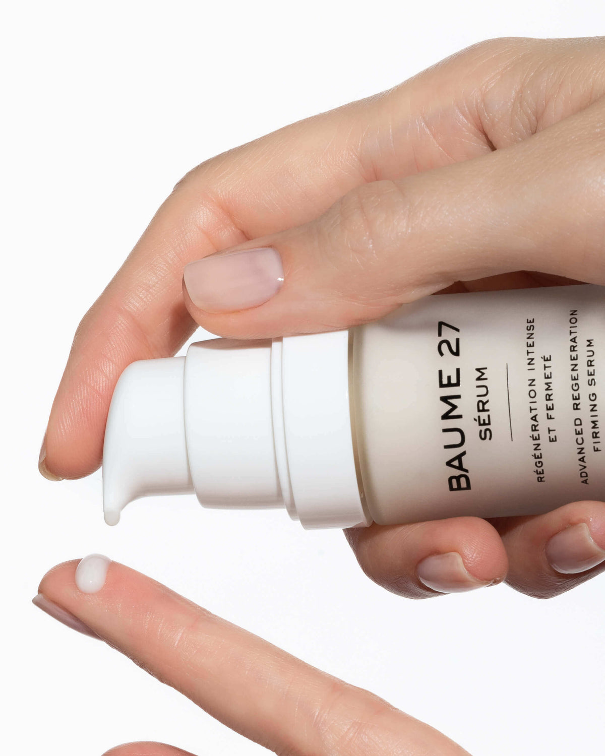 Hand pressing the pump of a Baume 27 Serum bottle, with a drop on a fingertip