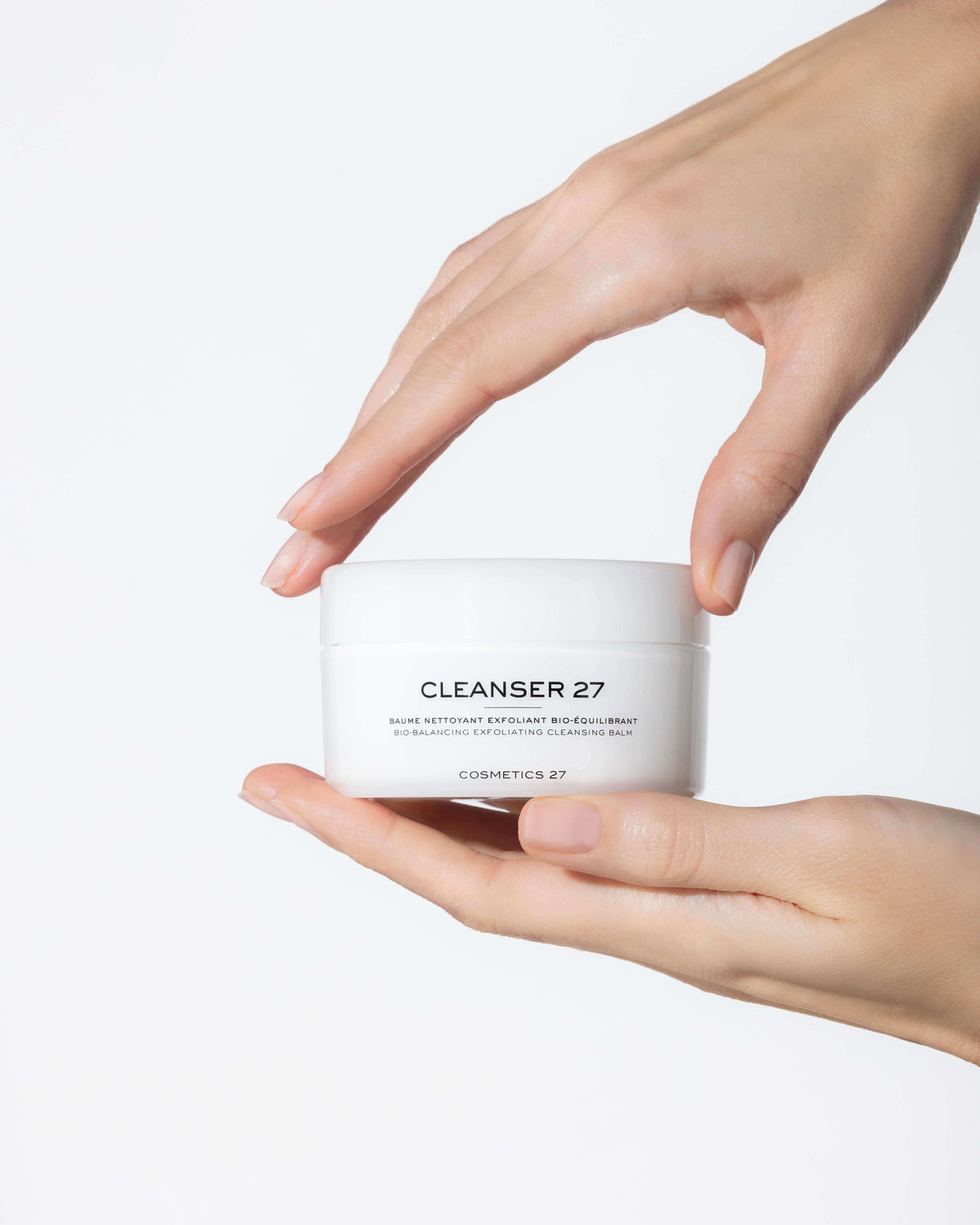 Two hands holding a jar of Cleanser 27, one from above and one from below