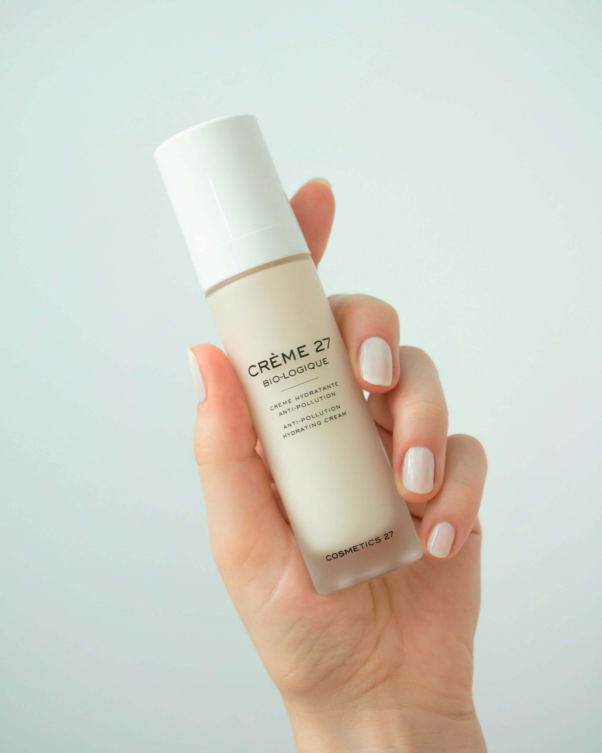 Hand holding a Crème 27 Bio-logique bottle against a pale aqua background