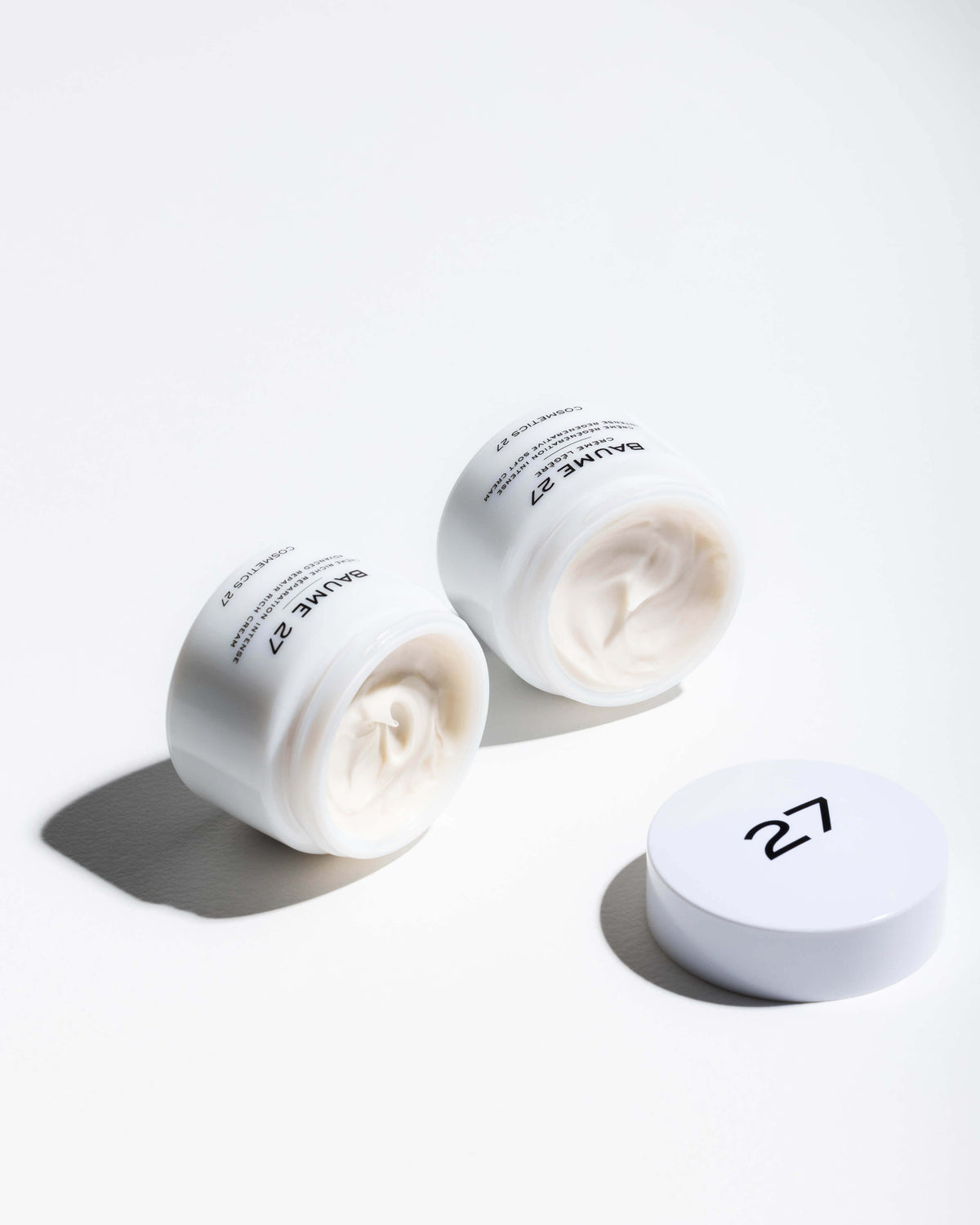Two open jars of Baume 27 Soft Cream lying on their sides, a "27" lid beside them
