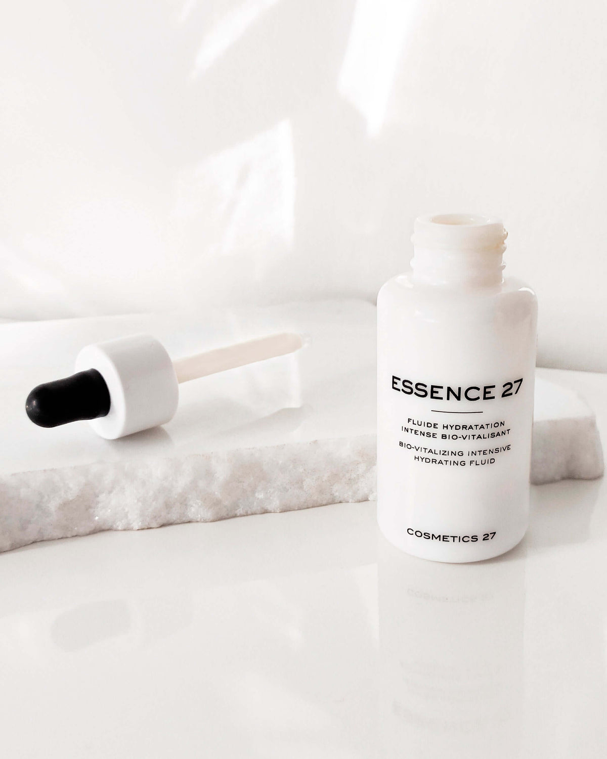 Open Essence 27 bottle, its dropper resting on a white marble block