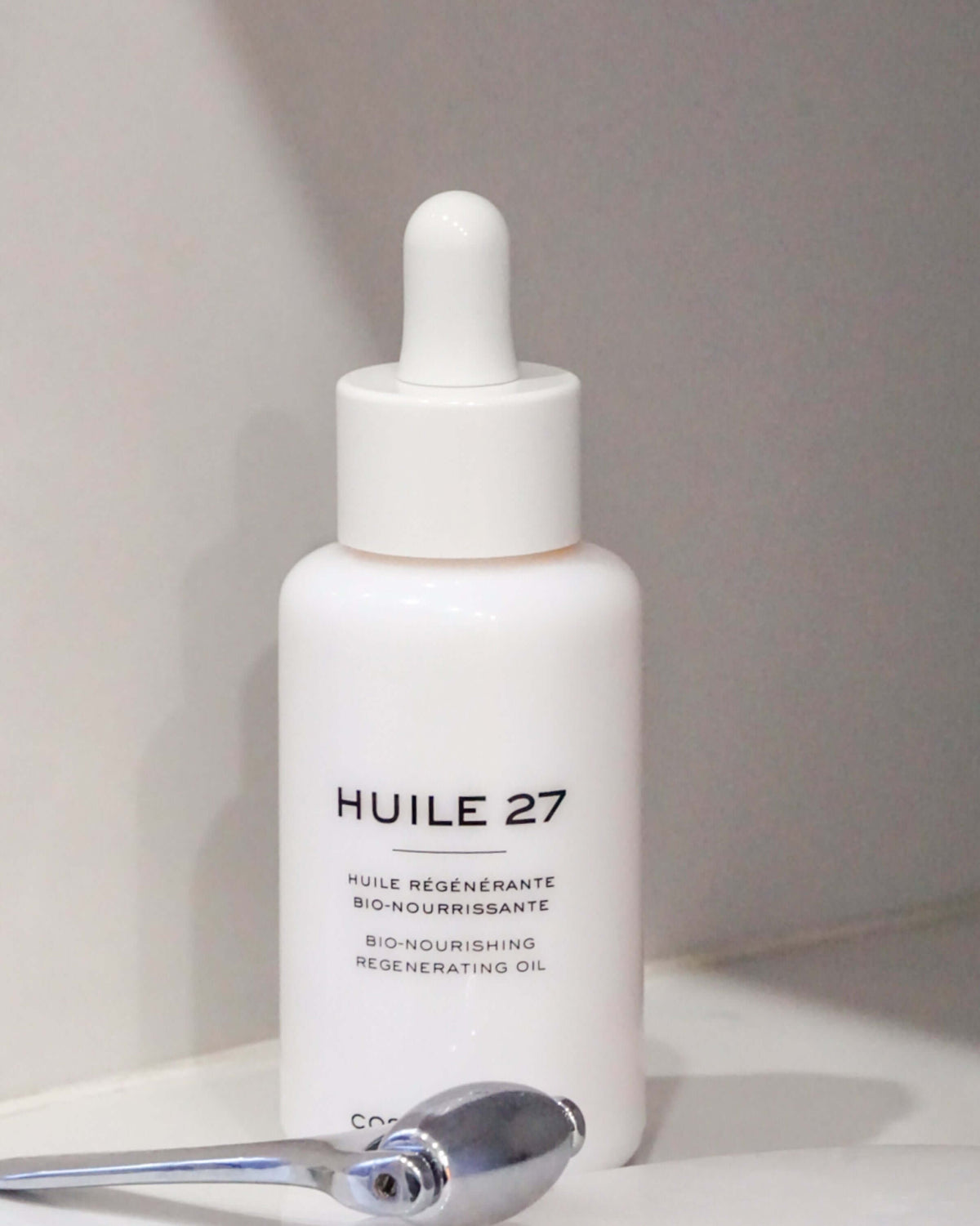 Flacon d'Huile 27 sur une tablette blanche, à côté d'un rouleau de massage en métal