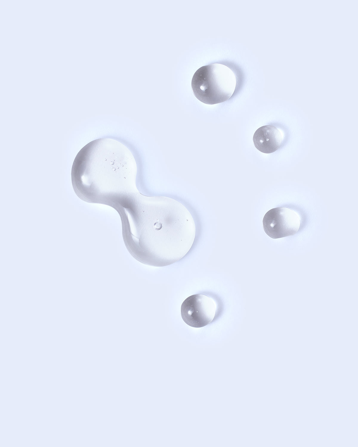 Gouttes de lotion transparente sur fond bleu pâle, montrant la texture