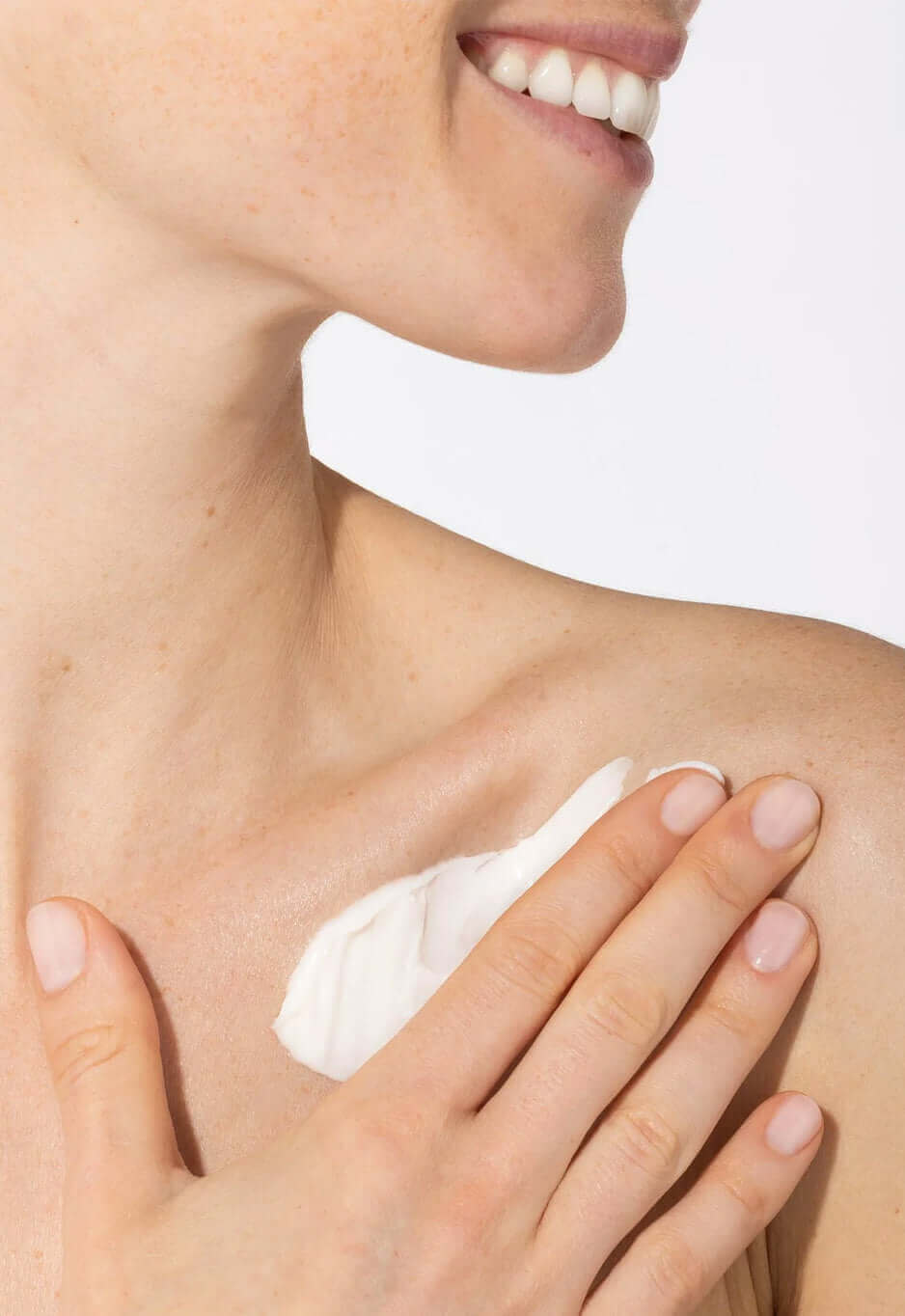 Smiling woman applying white cream to her shoulder near the collarbone
