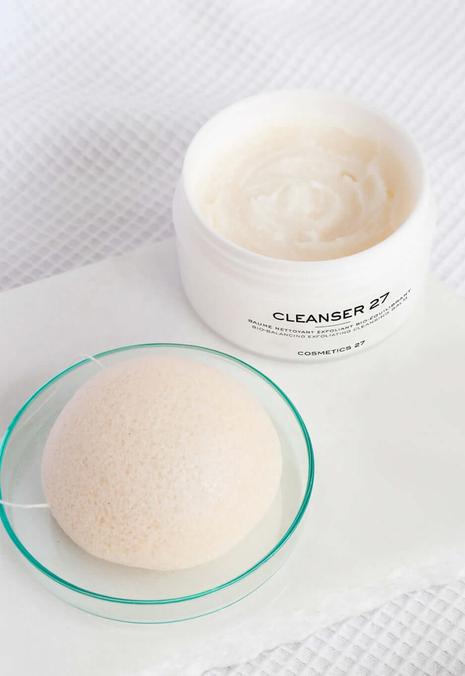 Éponge Konjac dans une coupelle en verre, à côté d'un pot ouvert de Cleanser 27